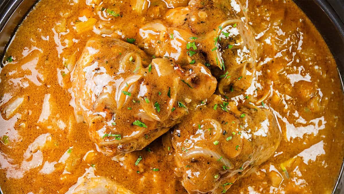 Close-up of a rich, creamy curry dish with chunks of chicken, garnished with chopped green herbs. The sauce is thick and velvety, dotted with pieces of onion, evoking a hearty and flavorful appearance reminiscent of Southern food comforts.