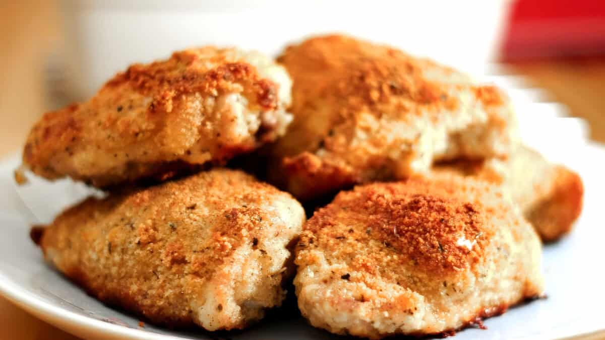 A plate of crispy, golden-brown fried chicken pieces is shown, epitomizing Southern Comfort Foods. The chicken appears to be seasoned with a variety of herbs and spices, giving the exterior a textured and flavorful crust. The background is blurred out, drawing focus to the appetizing chicken.