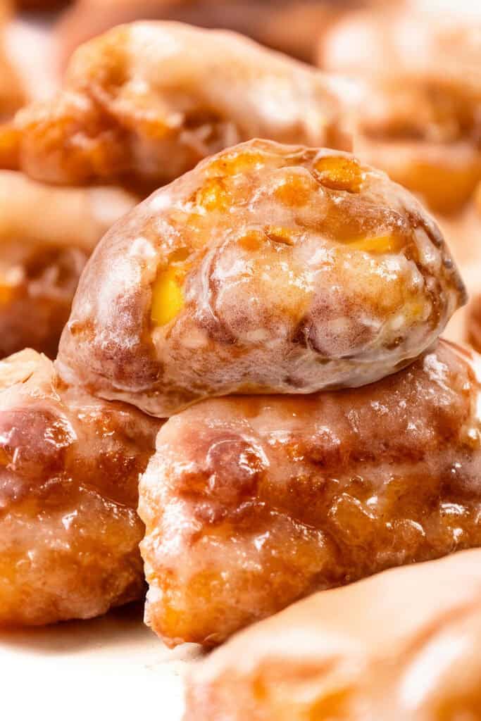 Close-up of delectable apple fritters stacked together. These golden brown delights boast a shiny glaze and visible chunks of apple, offering a textured and appetizing appearance.