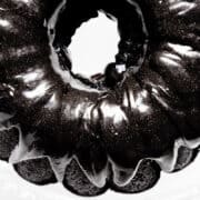 A shiny black velvet bundt cake with a glossy glaze is seen from above. The cake has a rich, dark color, and its smooth surface reflects light, creating an elegant visual effect on a white background.