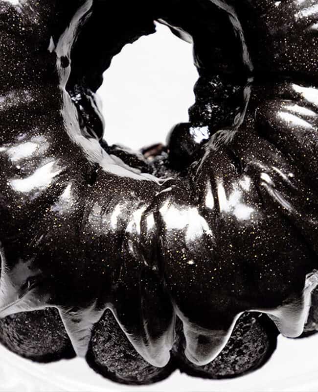 A shiny black velvet bundt cake with a glossy glaze is seen from above. The cake has a rich, dark color, and its smooth surface reflects light, creating an elegant visual effect on a white background.