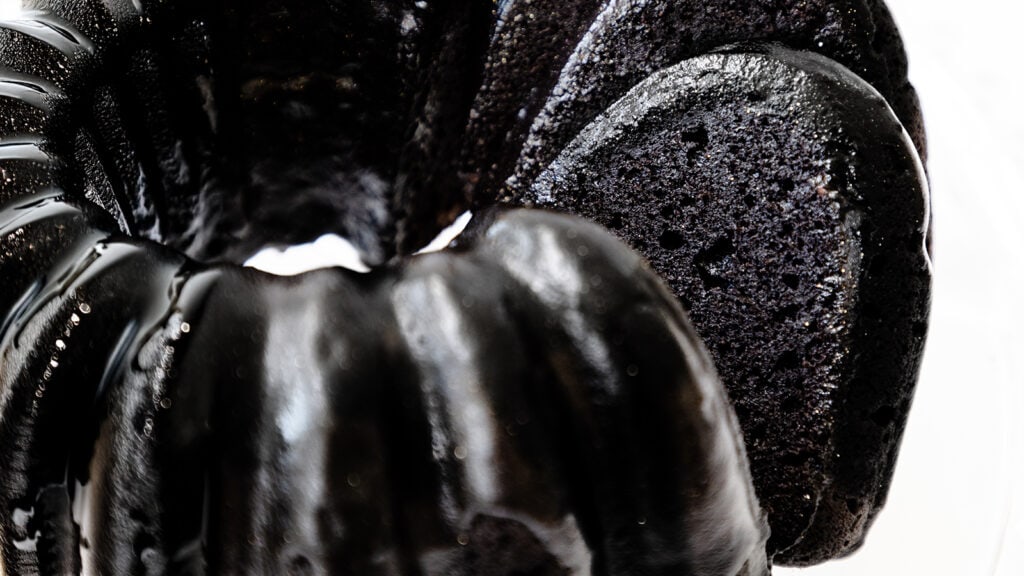 Close-up of a sliced black bundt cake with a glossy texture, perfect for those seeking to create show-stopping cakes. The image highlights its rich, dark color and moist appearance, inspiring you to make at home.