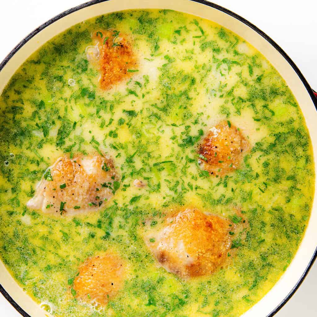 A pot of creamy soup with golden-brown chicken pieces and tender dumplings, topped with chopped green herbs. The vibrant yellow-green color suggests a blend of fresh ingredients.