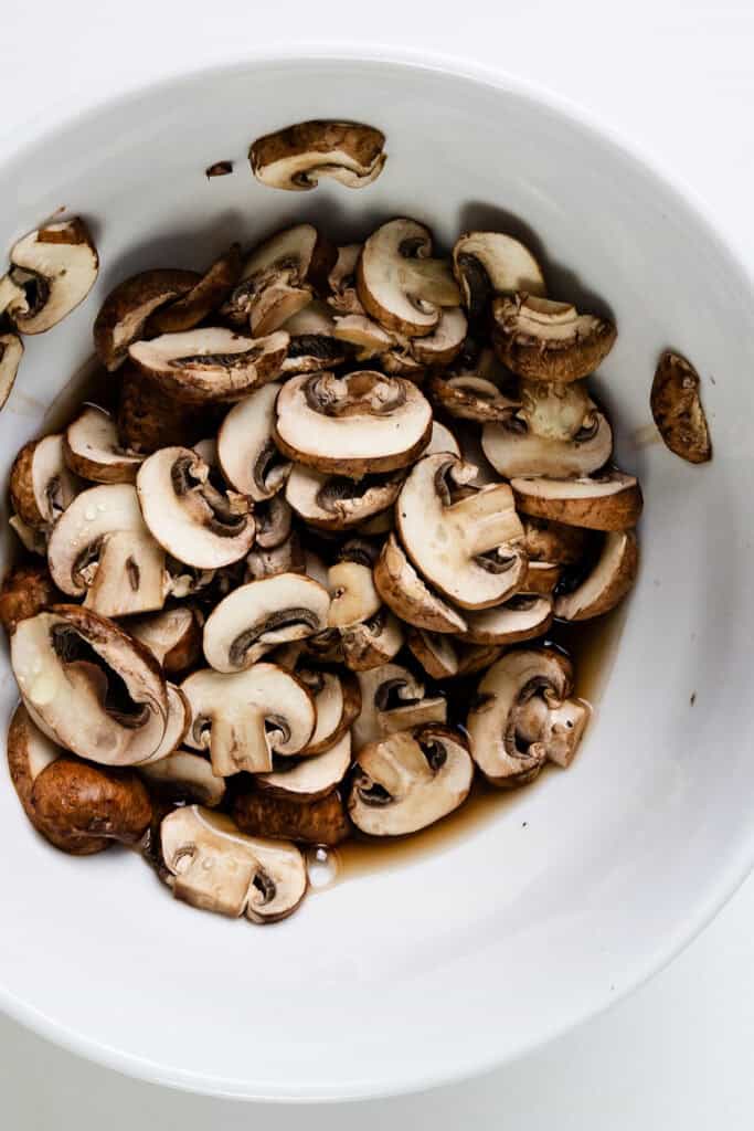 Sliced mushrooms in a white bowl on a white surface, perfect for a creamy Hamburger Stroganoff. The mushrooms appear fresh, offering a delightful mix of light and brown hues, ideal for your next comforting one-pot meal.