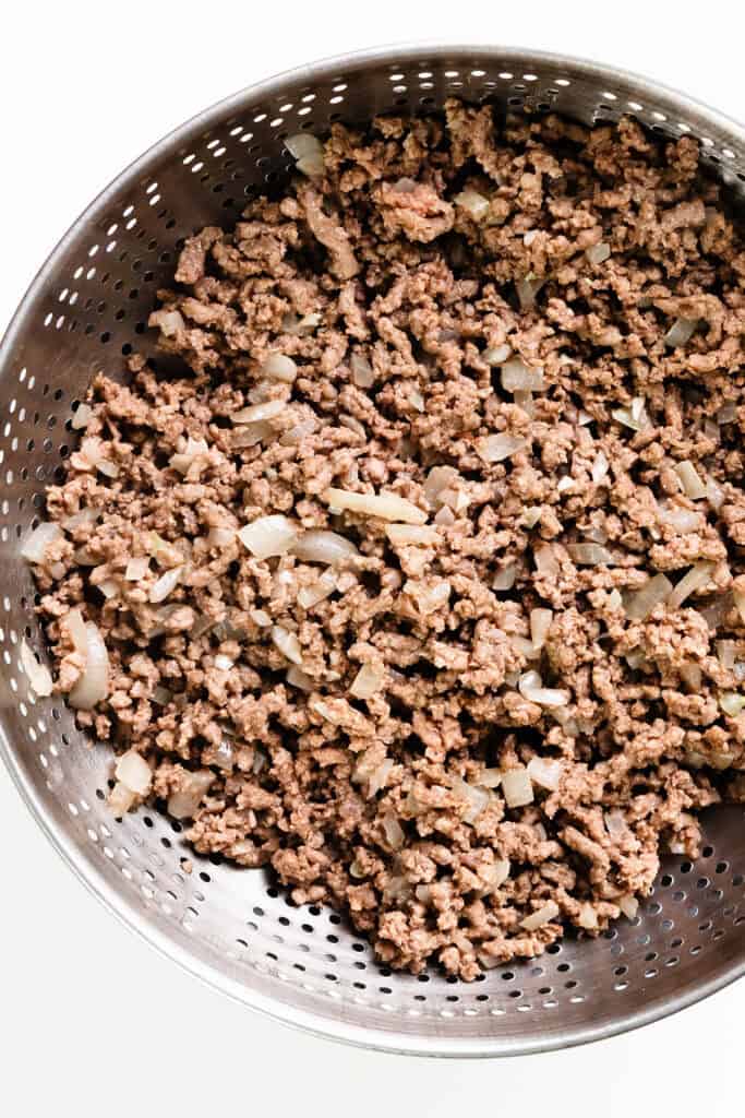 Cooked ground beef with diced onions in a stainless steel colander, perfect for starting your one-pot Hamburger Stroganoff.