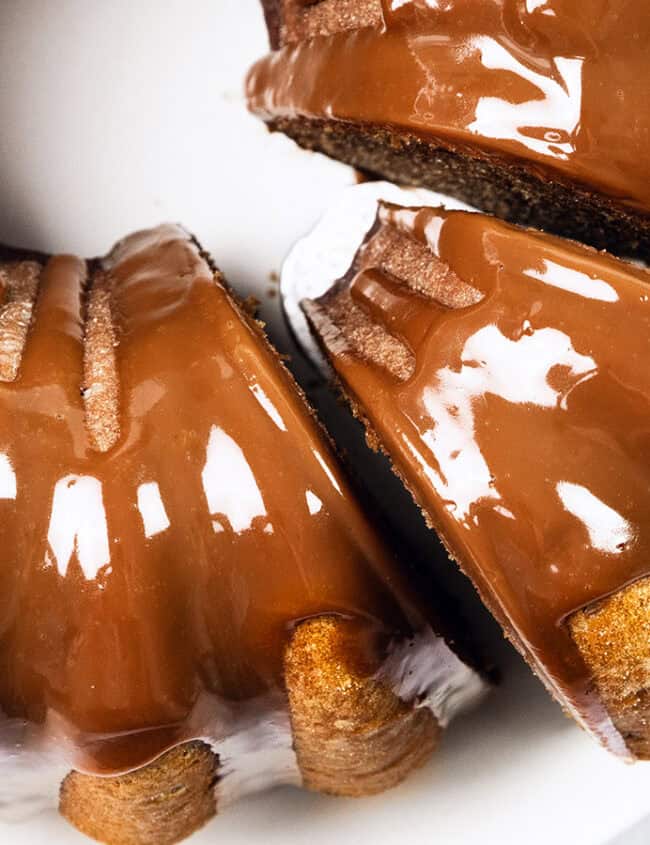 A bundt cake covered in glossy chocolate glaze, with a slice being lifted out on a spatula. The cake is on a white plate and the glaze appears smooth and rich.