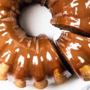 A close-up view of a delectable chocolate-glazed bundt cake, now irresistibly paired with a hint of pumpkin. One slice is partially removed, revealing the glossy glaze that reflects light and highlights the cake's rich texture.