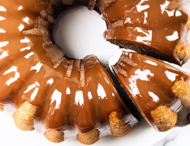 A close-up view of a delectable chocolate-glazed bundt cake, now irresistibly paired with a hint of pumpkin. One slice is partially removed, revealing the glossy glaze that reflects light and highlights the cake's rich texture.