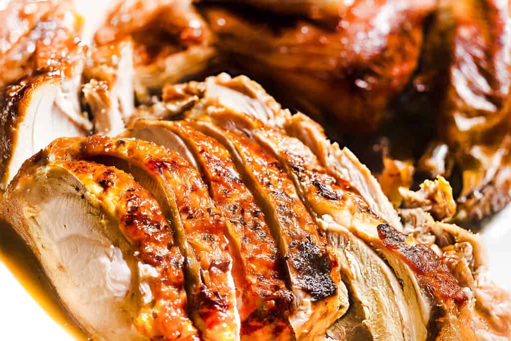 Close-up of slow-roasted turkey breast with golden, crispy skin and juicy white meat, served on a plate. The texture and browning highlight the turkey's tenderness and seasoning.