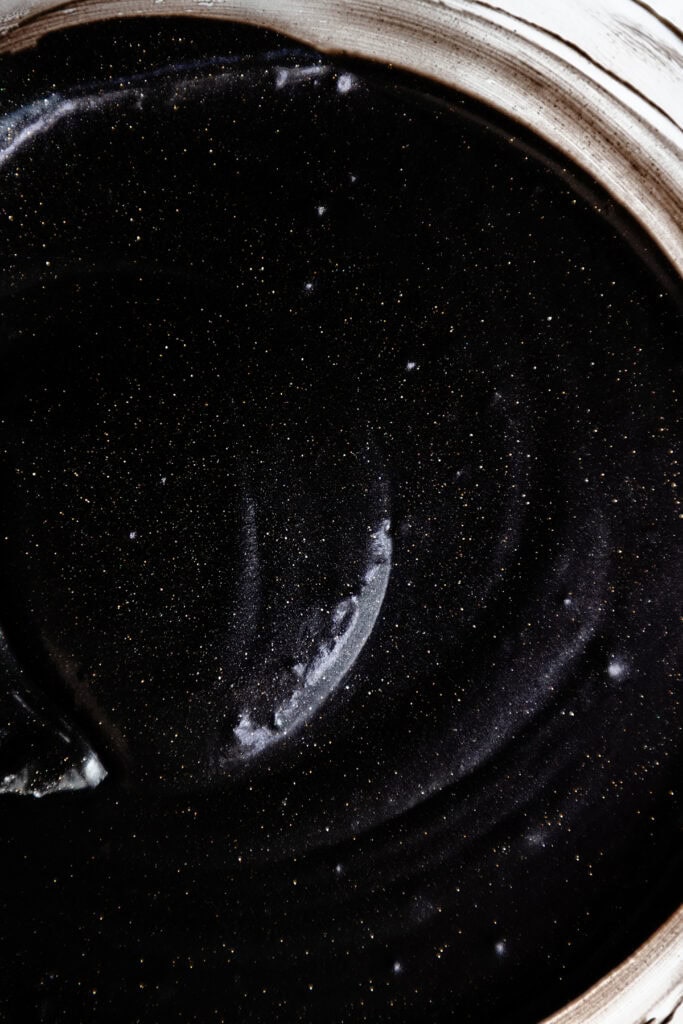 A close-up of a shiny, swirling black cake glaze with shimmering gold specks, resembling a night sky.