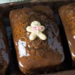 Three glazed gingerbread loaves, topped with tiny gingerbread men decorations, each adorned with colorful candy ties. These irresistible desserts are arranged in a row on a tray—perfect for those who simply can't get enough of holiday treats.