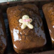 Three glazed gingerbread loaves, topped with tiny gingerbread men decorations, each adorned with colorful candy ties. These irresistible desserts are arranged in a row on a tray—perfect for those who simply can't get enough of holiday treats.