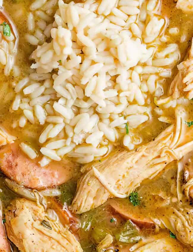 A bowl of gumbo featuring shredded chicken, sliced sausage, okra, and a scoop of white rice. The dish is garnished with herbs, set in a savory broth, capturing a hearty and comforting meal.