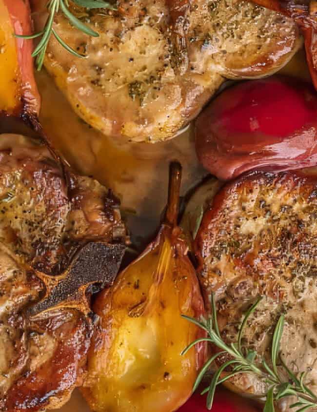 A cast iron skillet holds roasted pork chops with red and orange peppers, halved pears, and sprigs of fresh rosemary. This is one of those fall recipes that embraces cozy flavors in every bite.