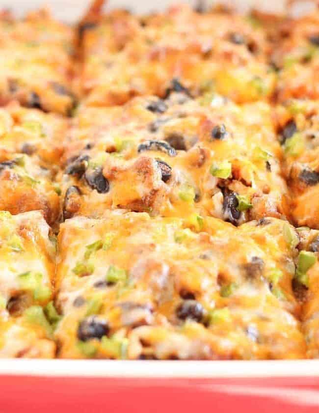 A close-up of an irresistible baked dish in a red casserole dish, featuring golden-brown cheesy squares with toppings of black olives and green peppers. The dish appears freshly baked and ready to serve, making it one you'll want to make again.