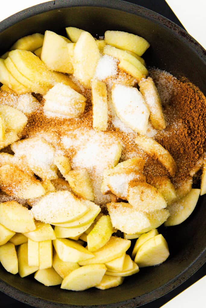 A close-up of sliced apples and pears in a pan, mixed with sugar and cinnamon, ready for cooking into a delicious pie filling.