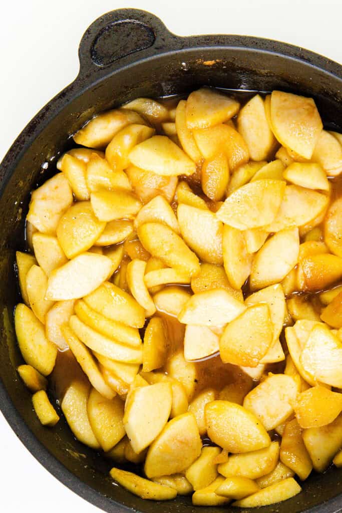 Sliced apples and juicy pears coated in a golden-brown sauce fill a black cast iron skillet, ready for baking into a delightful pie or serving as is.