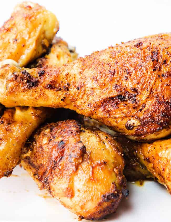 A plate of crispy, golden-brown fried chicken drumsticks piled high, seasoned with herbs and spices, on a white plate.