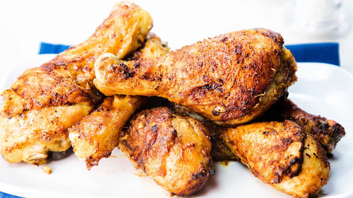 A plate of crispy, golden-brown fried chicken drumsticks piled high, seasoned with herbs and spices, on a white plate.