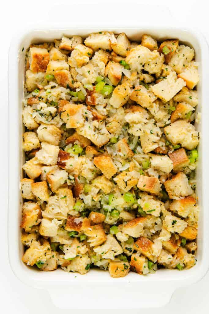 A rectangular white dish filled with make-ahead herb stuffing. The seasoned stuffing consists of toasted bread cubes mixed with chopped celery, onions, and herbs, giving it a textured and golden-brown appearance.