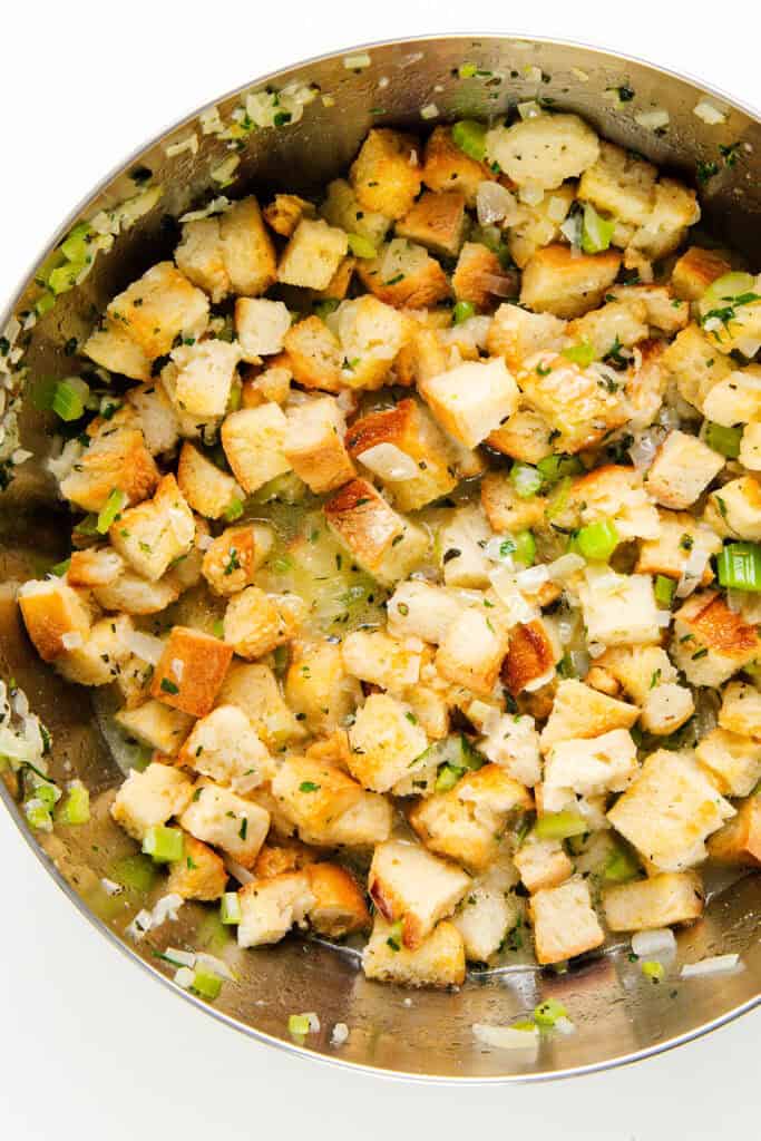 A skillet filled with cubed bread pieces, mixed with chopped celery, onions, and herbs, creates a savory herb stuffing mixture. Perfect as a make-ahead stuffing recipe for any occasion.