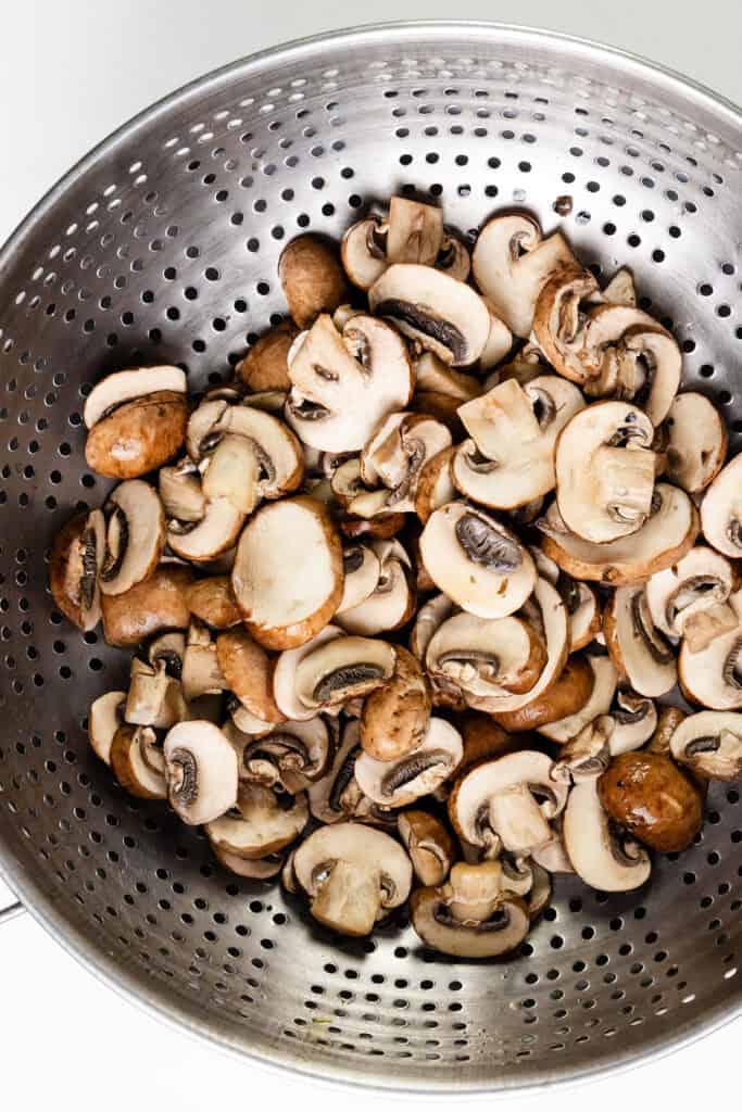 A metal colander brimming with sliced brown mushrooms hints at the beginning of a turkey casserole recipe. The fresh mushrooms, varied in size and sporting smooth, light brown caps and white interiors, rest atop the perforated surface, ready to unite with flavorful leftover turkey.