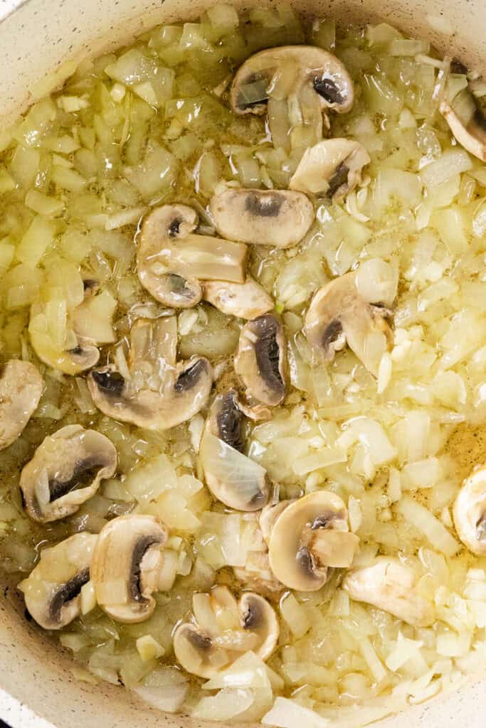 Chopped onions and sliced mushrooms sizzle in a pan with oil, lightly browning as they cook. The mixture is evenly spread across the bottom, ready to welcome chunks of leftover turkey for a flavorful twist on a classic dish.