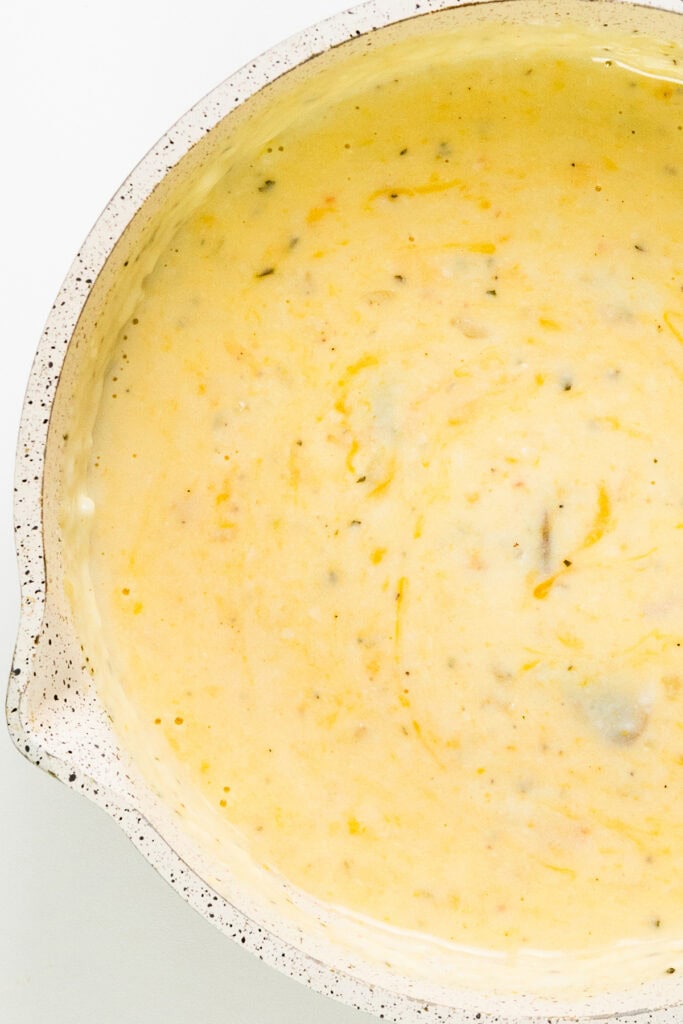 A close-up of a creamy soup in a speckled bowl showcases its smooth texture and small vegetable pieces. This leftover turkey-inspired dish contains vibrant herbs, with light yellow tones and orange and green flecks, giving it an appealing casserole-like appearance.