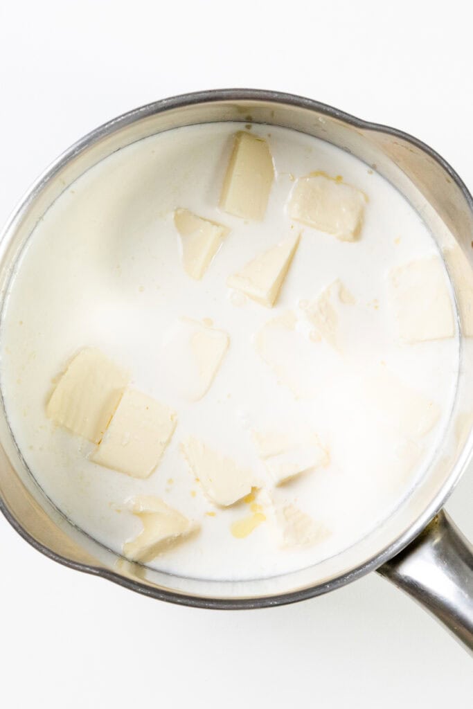 A pot with milk and chunks of butter melting inside, perfect for prepping make-ahead mashed potatoes, viewed from above on a white background.