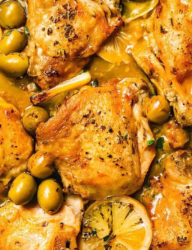 Close-up of a skillet showcasing a tried-and-true recipe with roasted chicken thighs, sliced lemons, and green olives. The dish appears to be seasoned with herbs and spices, hitting the mark with its golden-brown finish and savory, well-cooked appearance.