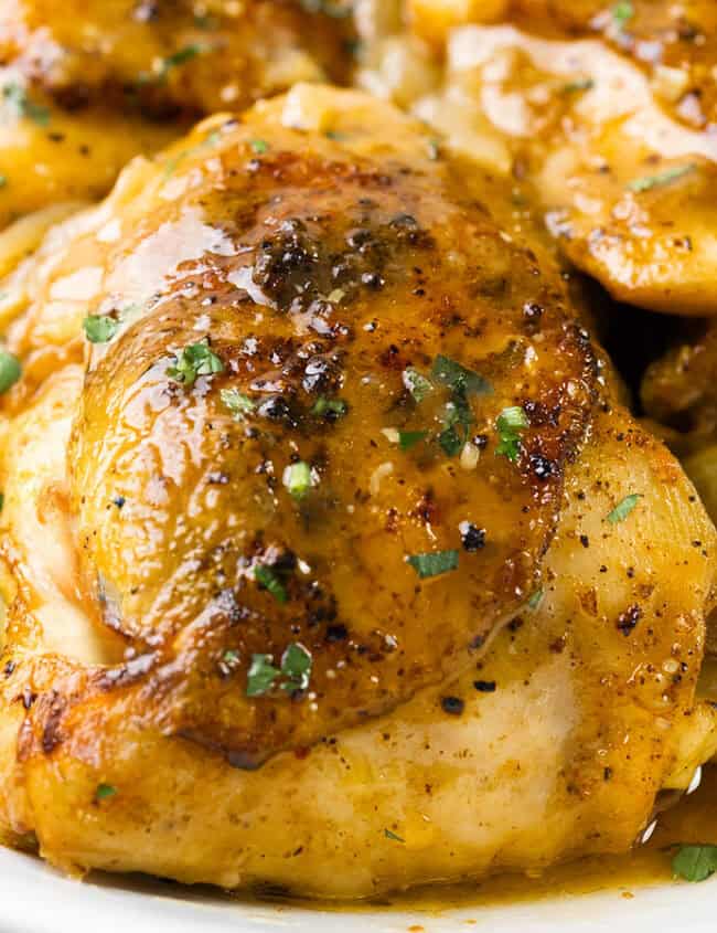 A close-up of seasoned, cooked chicken pieces served in a flavorful sauce with olives and lemon slices, garnished with fresh herbs—true comfort food at its finest.