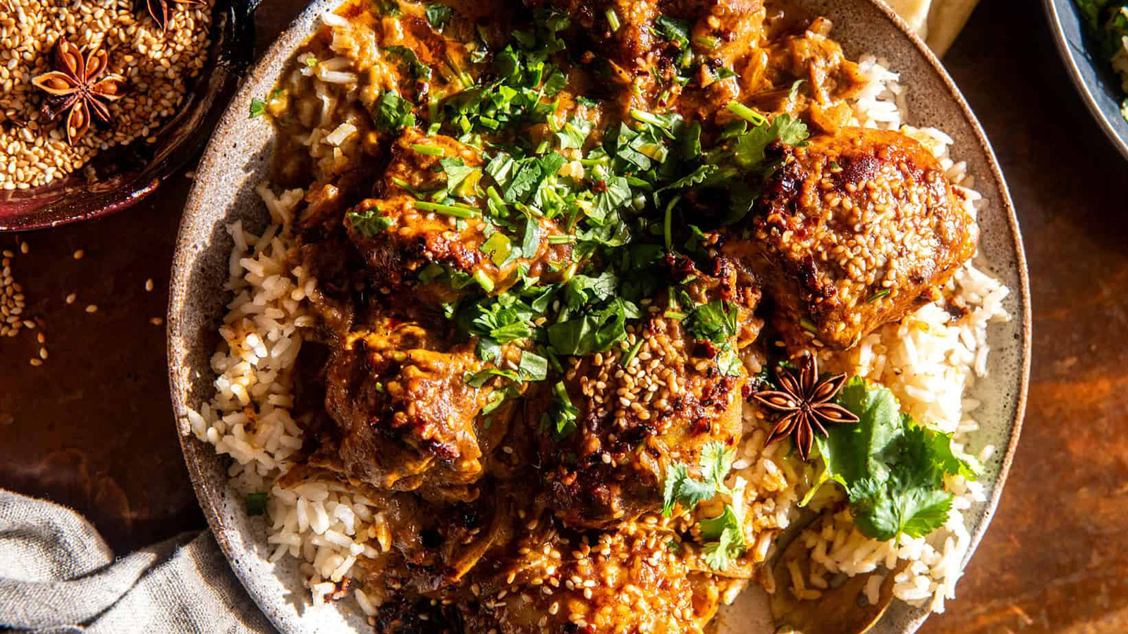 A plate of rice topped with spiced curry, garnished with fresh cilantro and sesame seeds. The dish is surrounded by star anise, enhancing its visual appeal with a warm and inviting aura.