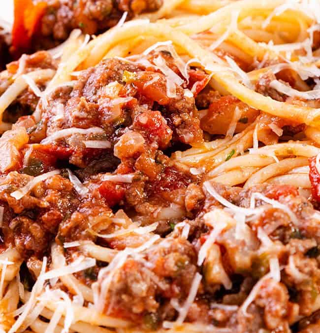 A close-up of spaghetti bolognese topped with grated cheese highlights this classic ground beef recipe. The dish features spaghetti noodles mixed with a savory meat and tomato sauce, garnished with shredded cheese, creating a hearty and appetizing appearance.