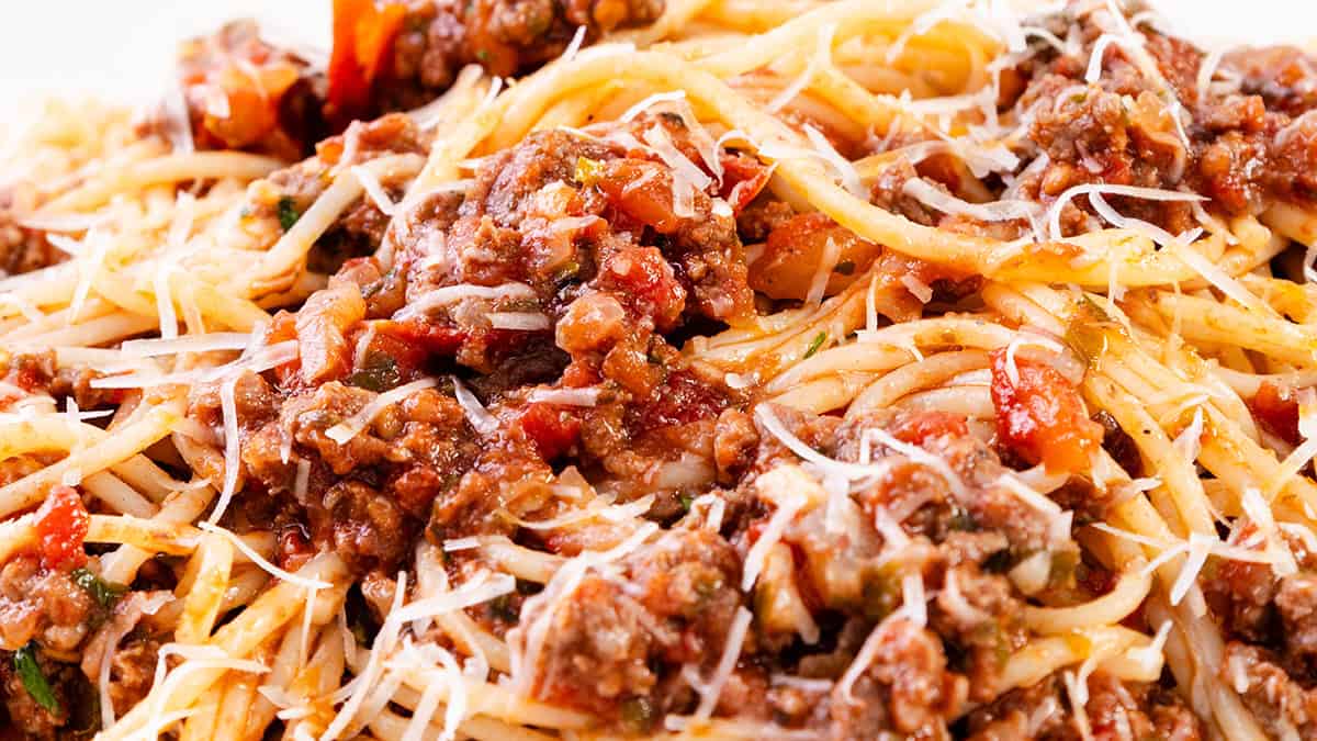 A close-up of spaghetti bolognese topped with grated cheese highlights this classic ground beef recipe. The dish features spaghetti noodles mixed with a savory meat and tomato sauce, garnished with shredded cheese, creating a hearty and appetizing appearance.