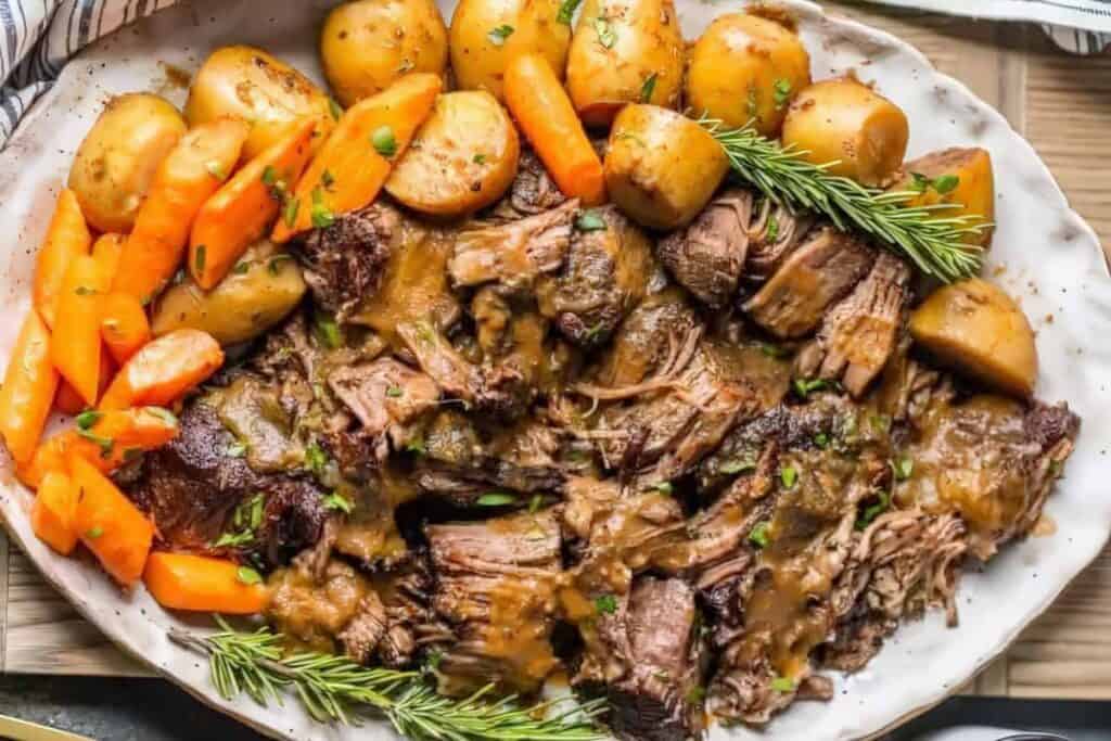 A platter of tender braised beef pot roast, surrounded by roasted carrots, potatoes, and garnished with rosemary sprigs. Reminiscent of classic ground beef recipes, this dish is drenched in savory gravy, creating a comforting and hearty feast.