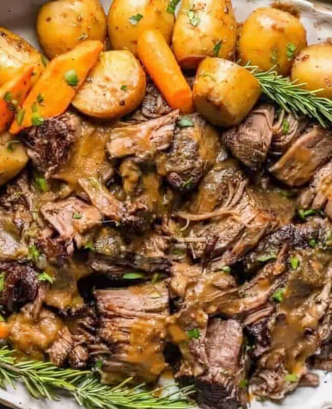 A platter of tender braised beef pot roast, surrounded by roasted carrots, potatoes, and garnished with rosemary sprigs. Reminiscent of classic ground beef recipes, this dish is drenched in savory gravy, creating a comforting and hearty feast.