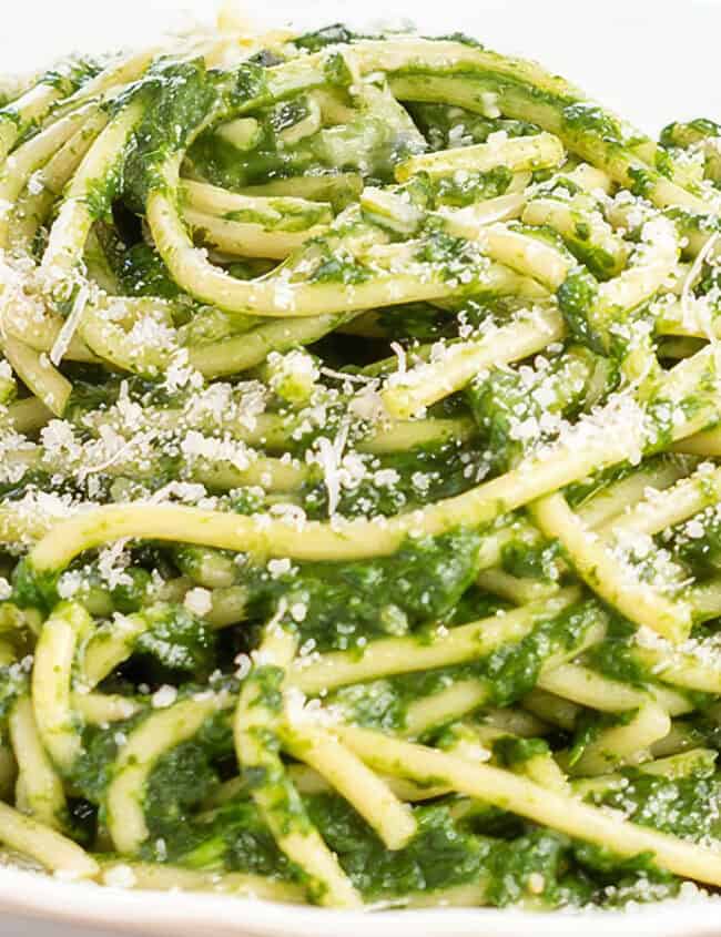 A bowl of spaghetti coated in a creamy green spinach sauce, topped with a sprinkle of grated cheese, makes this tried-and-true recipe a hit. The pasta is served elegantly in a white dish.