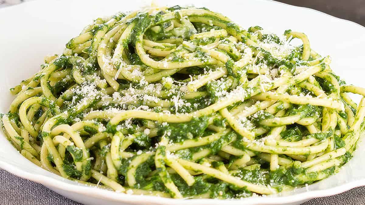 A bowl of spaghetti coated in a creamy green spinach sauce, topped with a sprinkle of grated cheese, makes this tried-and-true recipe a hit. The pasta is served elegantly in a white dish.