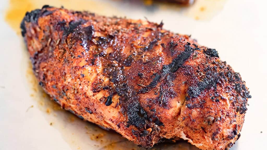 Grilled, seasoned chicken breast on a white surface, showcasing enticing grill marks and a crispy exterior—a nod to traditional Southern cooking.