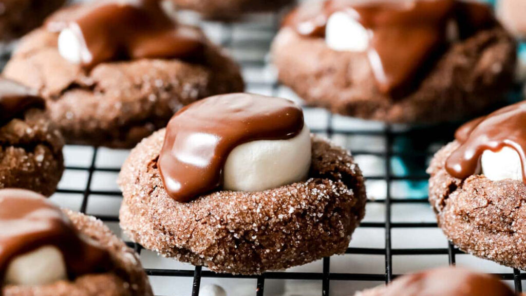 A close-up of chocolate cookies on a cooling rack, each topped with a marshmallow and covered in melted chocolate, glistening under light—a perfect treat for holiday baking or an indulgent addition to your favorite cookie recipes.