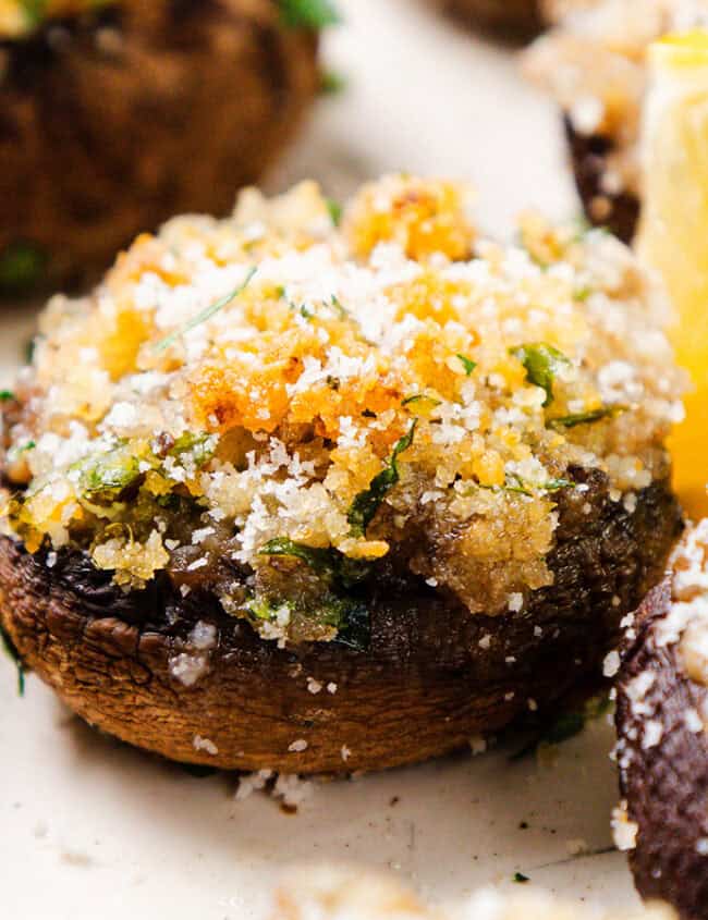 Stuffed mushrooms topped with breadcrumbs and herbs are garnished with parsley and a slice of lemon on the side, making them an ideal party food. Perfect for New Year's festivities, this baked dish boasts a crispy golden-brown crust that pairs wonderfully with various dips.