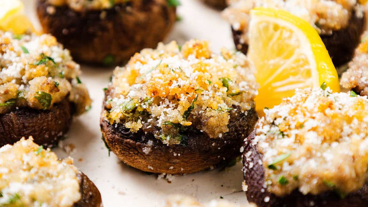 Stuffed mushrooms topped with breadcrumbs and herbs are garnished with parsley and a slice of lemon on the side, making them an ideal party food. Perfect for New Year's festivities, this baked dish boasts a crispy golden-brown crust that pairs wonderfully with various dips.