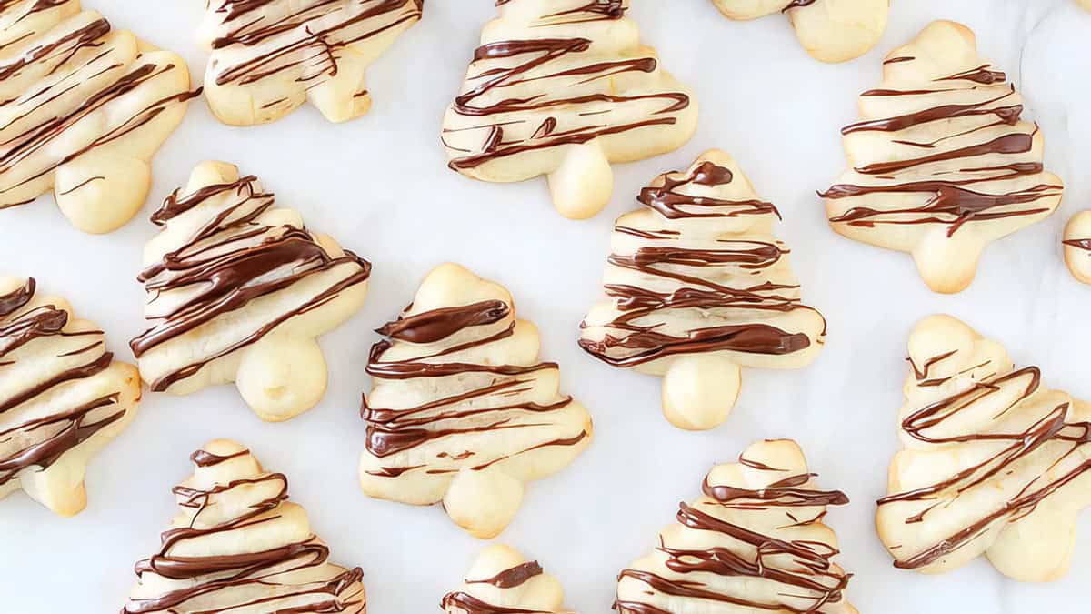 Christmas tree-shaped sugar cookies, delightful holiday treats, are drizzled with chocolate and artfully arranged on a pristine white surface.