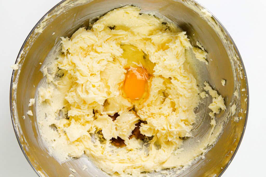 A metal mixing bowl holds a creamy butter and sugar mixture with an egg yolk nestled at its center. The partially blended ingredients hint at the delightful beginnings of Italian Pinch Cookies, setting the stage for a baking masterpiece.