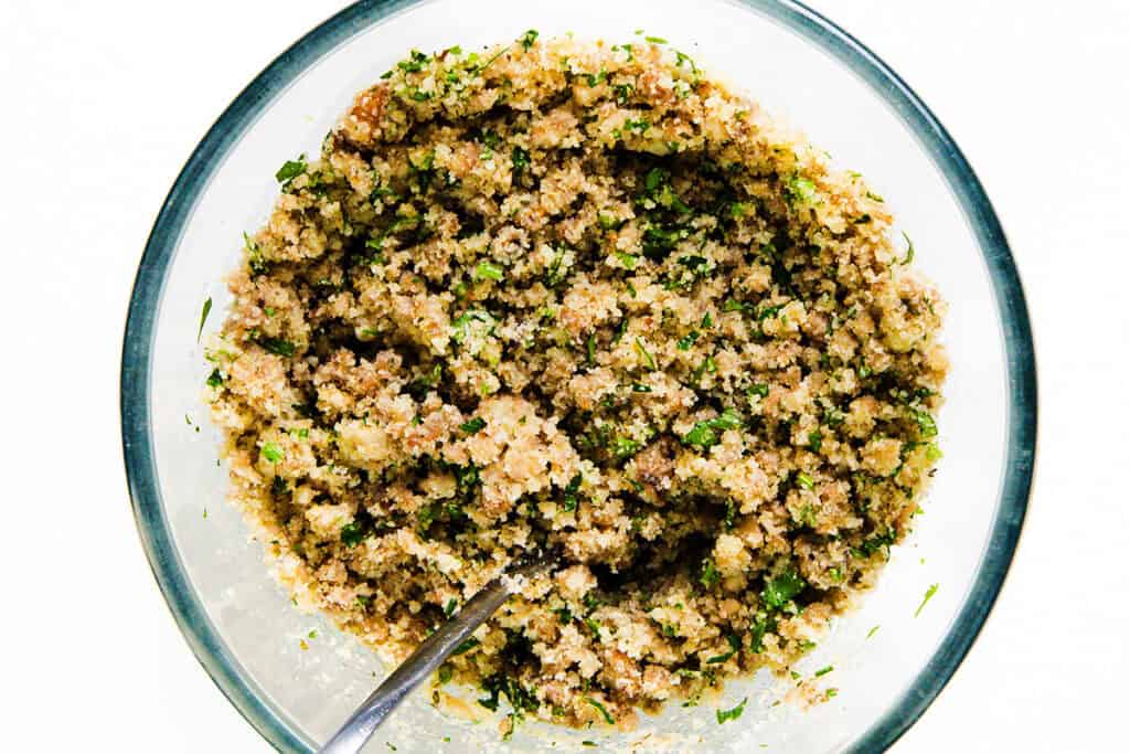 A glass bowl filled with seasoned quinoa mixed with finely chopped herbs sits ready for serving, perfect as a base for your favorite appetizer or a delightful stuffed mushrooms recipe. A spoon is placed in the bowl, inviting you to savor its freshness.