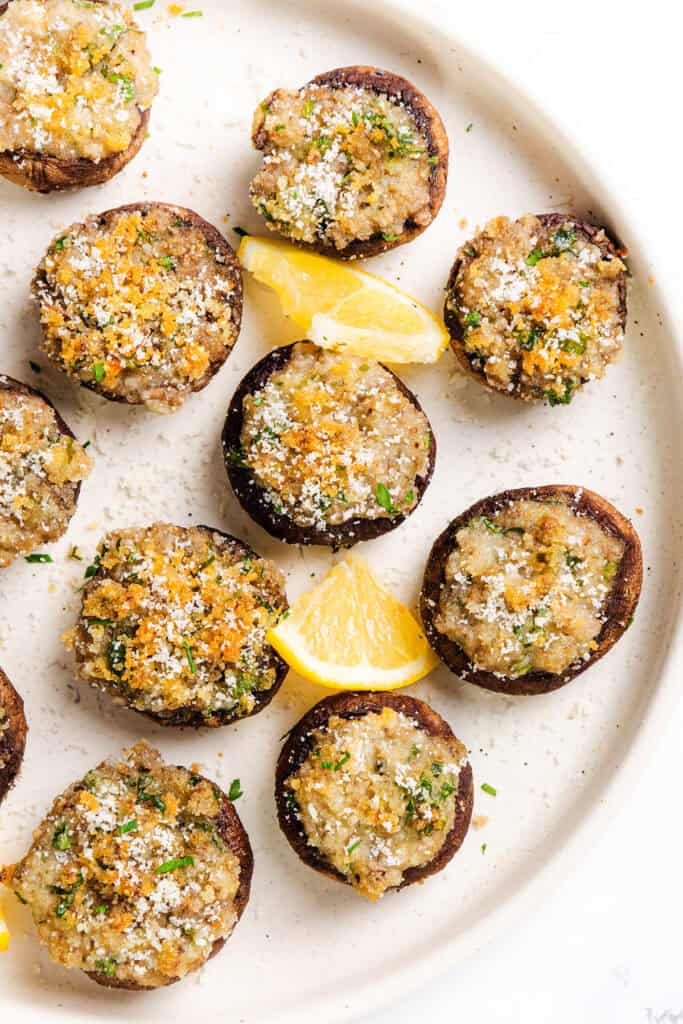 A delightful plate of stuffed mushrooms is garnished with golden breadcrumbs and fresh herbs, with lemon wedges nestled among them for an extra burst of flavor.