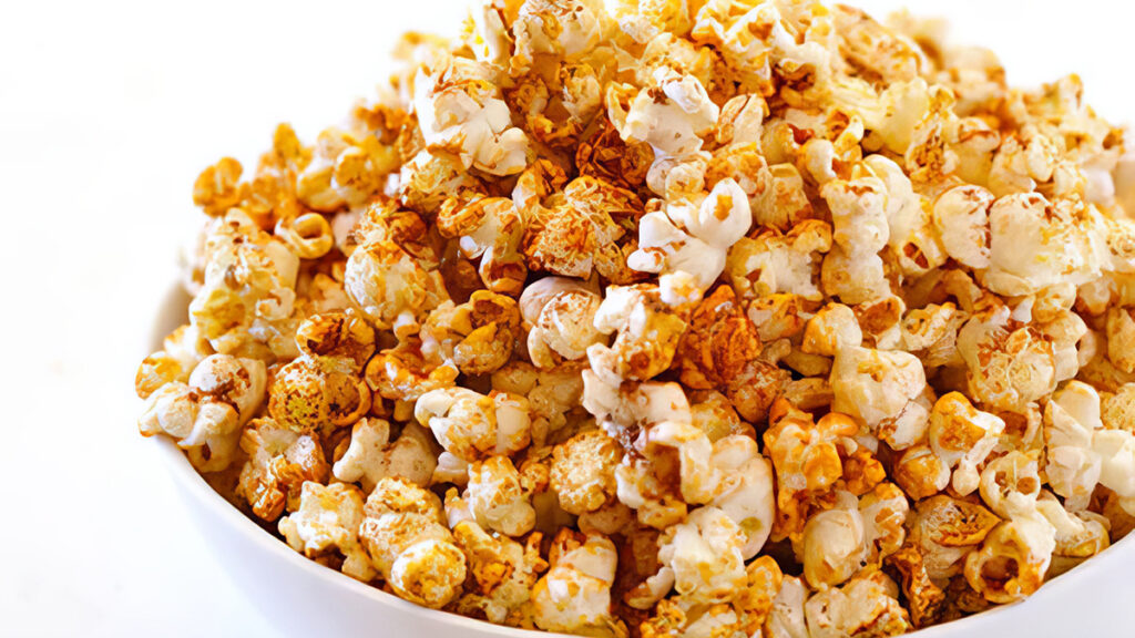 A white bowl filled with freshly popped popcorn, a delightful option for those exploring finger food recipes. Lightly sprinkled with a reddish seasoning, it's perfect for sharing on any casual occasion, all set against a crisp white background.