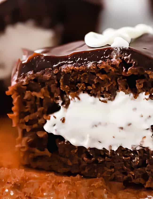 A chocolate cupcake sliced in half reveals a creamy white filling reminiscent of old-fashioned cakes. It's topped with glossy chocolate icing and a small white decorative swirl that keeps everyone coming back for more. It sits on an unwrapped paper liner, inviting indulgence.