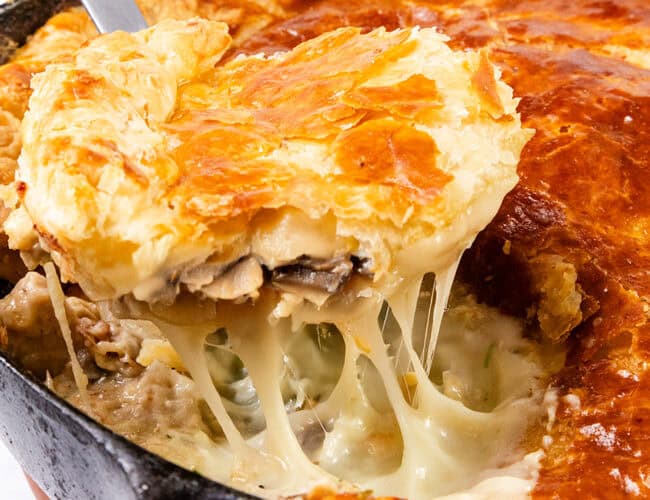 A close-up of a freshly baked pot pie in a skillet. A portion has been cut and lifted, revealing gooey melted cheese, flaky golden-brown crust, and creamy mushroom filling that rivals even the best chicken cutlet recipes in comfort and flavor.