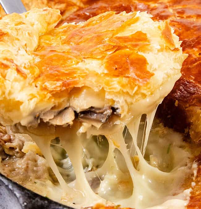 A close-up of a freshly baked pot pie in a skillet. A portion has been cut and lifted, revealing gooey melted cheese, flaky golden-brown crust, and creamy mushroom filling that rivals even the best chicken cutlet recipes in comfort and flavor.